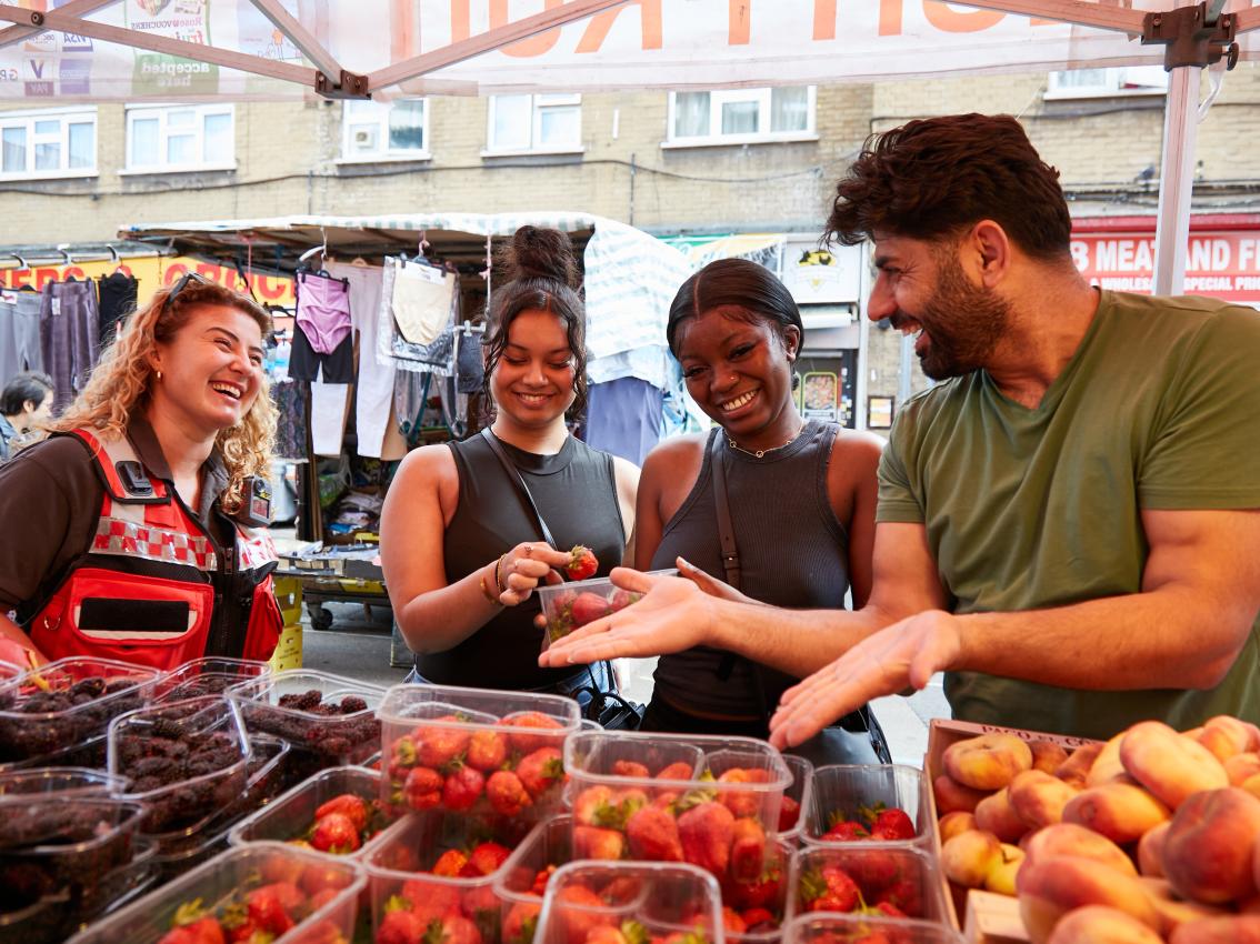 Four people at fruit stand in East Street Market Walworth