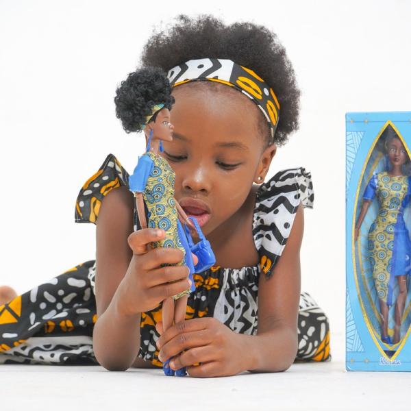 A young black girl playing with a Black doll, dressed in a costume made with African printed fabric