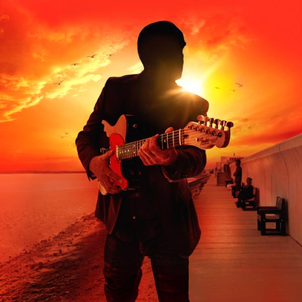 A man plays a guitar in front of a sunset.