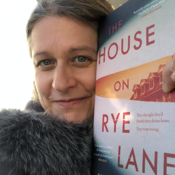 An image of author Susan Allott, holding up a copy of her novel 'The House on Rye Lane' next to her face