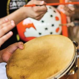 Close-up image of hands playing a tambourine and drums